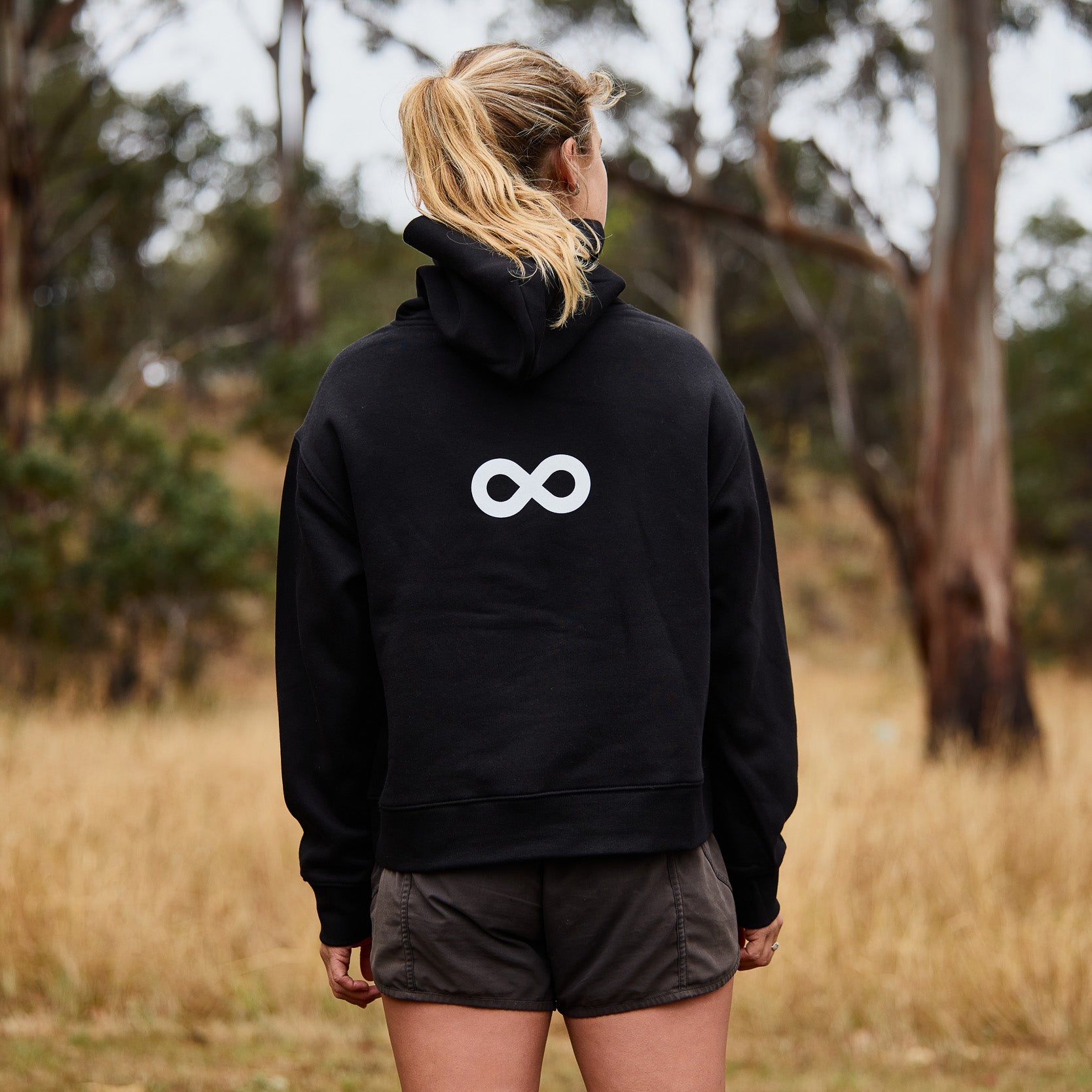 Person wearing a black hoodie with a white logo in a forest setting