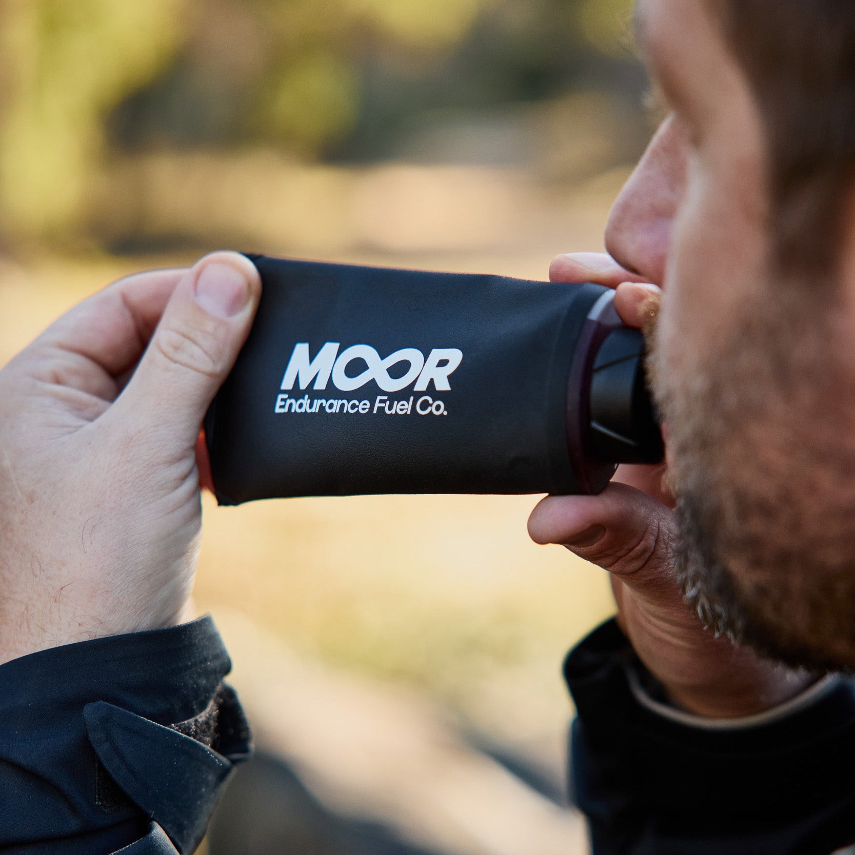 Person holding a black 'MOOR Endurance Fuel Co.' container outdoors.