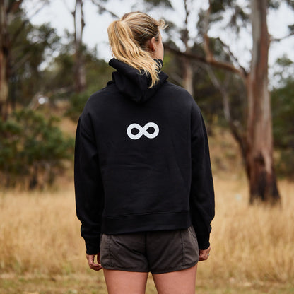 Person wearing a black hoodie with a white logo in a forest setting